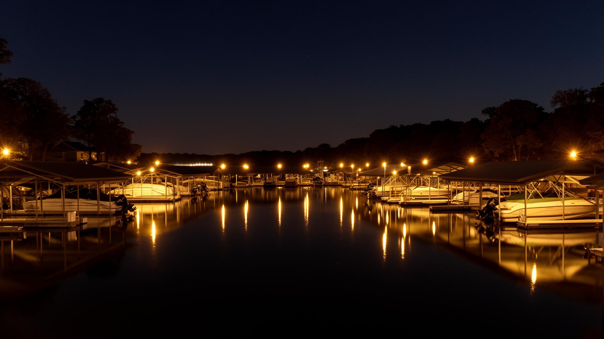The lighted marina at Spring Cove at night, boats in covered slips reflecting on calm water